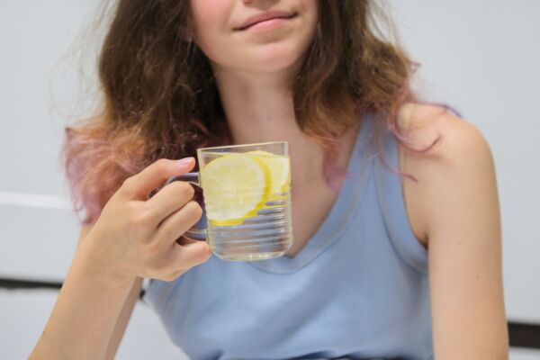 Girl sitting in bed with glass of water with lemon.