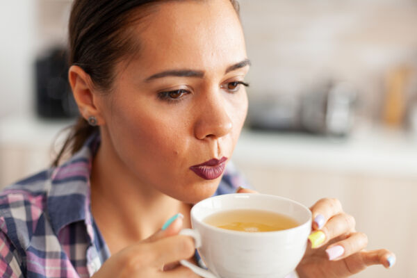 Close up of woman in kitchen trying to drink hot green tea with aromatic herbs. Pretty lady sitting in the kitchen in the morning during breakfast time relaxing with tasty bone broth