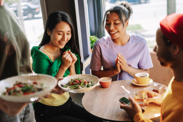 Diverse group of multinational friends enjoying a fresh salad in a trendy city cafe, smiling and chatting happily. Food concept